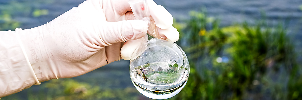 A scientist holds a beaker of water by a pond